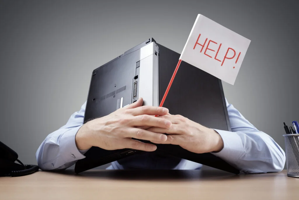 Frustrated and overworked businessman burying his head uner a  laptop computer asking for help