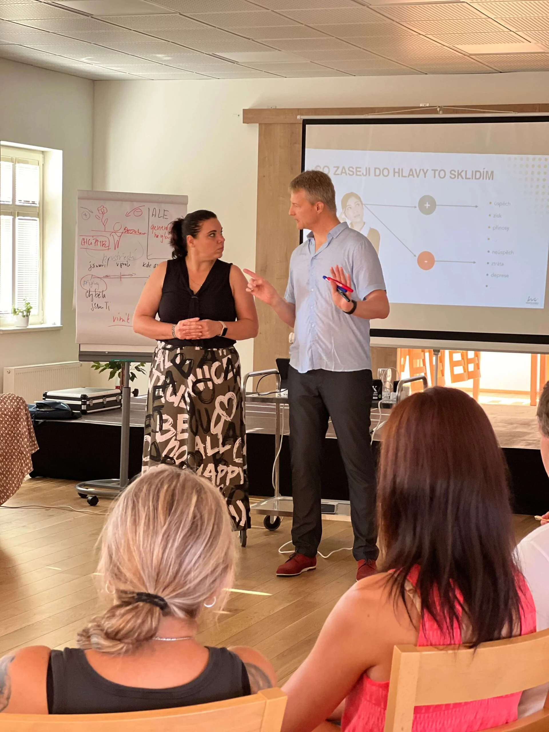 Lektor s účastnicí diskutují u flipchartu, znázorňují otevřenou atmosféru a praktické cvičení během kurzu.